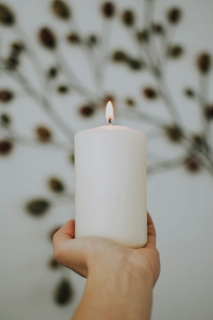 A hand holds a lit white candle against a blurred, artistic backdrop, creating a peaceful ambiance.